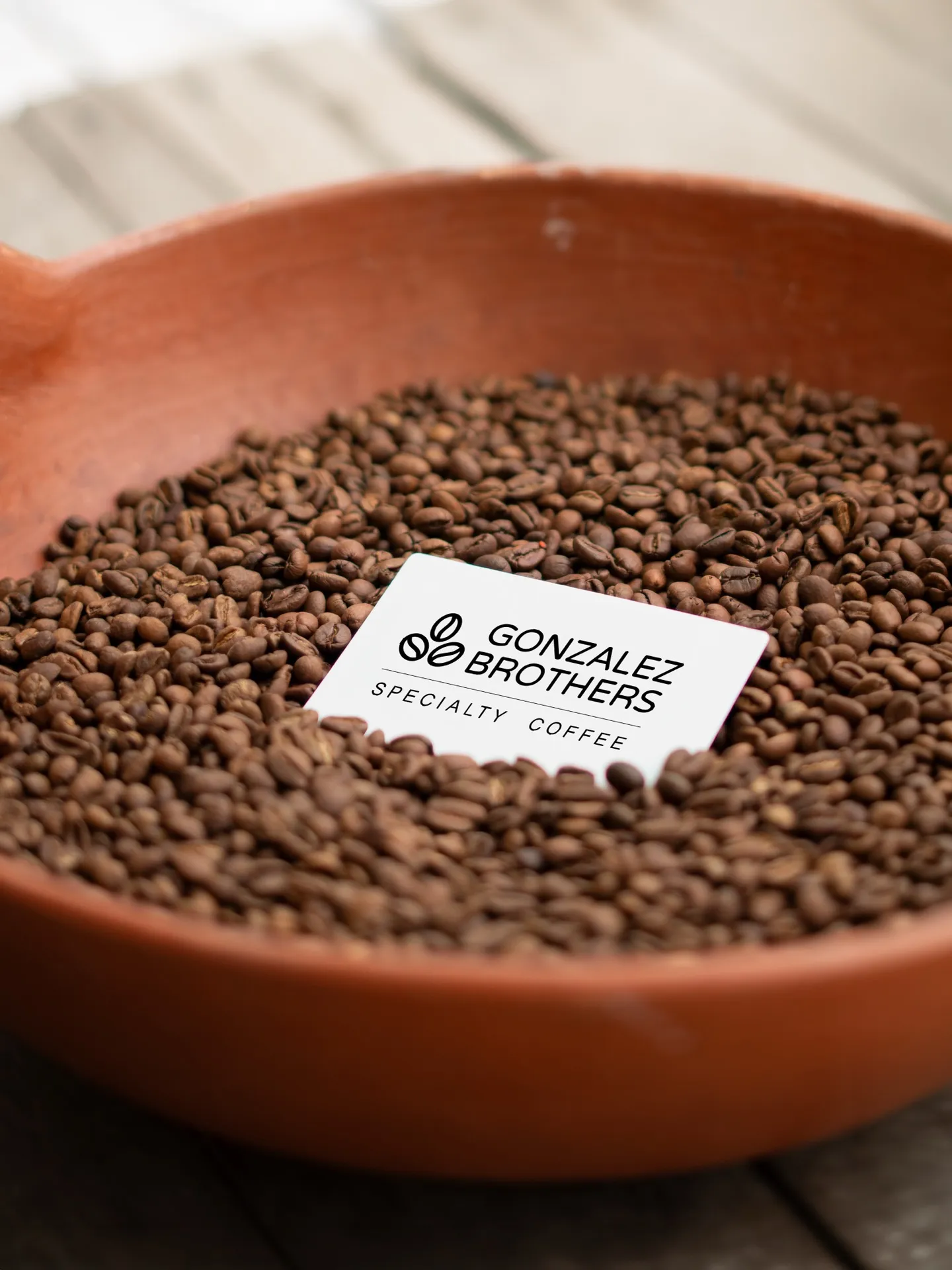 Freshly roasted Gonzalez Brothers coffee beans in a clay bowl with a branded card