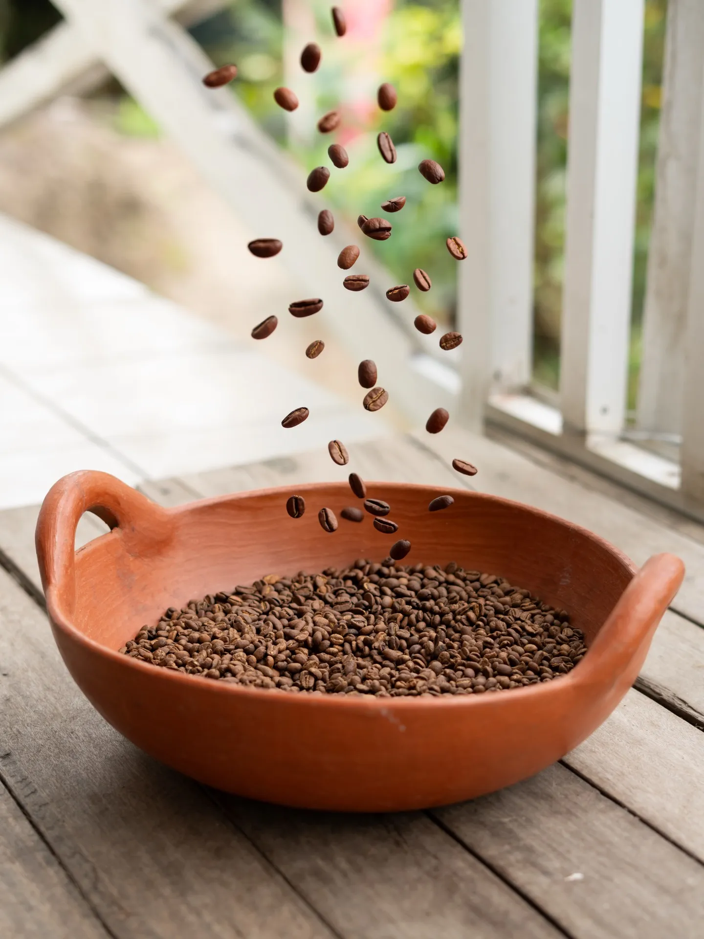 Roasted coffee beans falling into a clay bowl